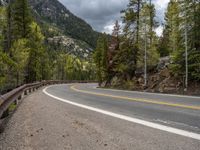 the curved road curves in front of a mountain area with pine trees behind it,