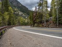 the curved road curves in front of a mountain area with pine trees behind it,