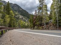 the curved road curves in front of a mountain area with pine trees behind it,