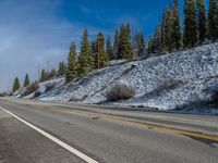 a lone motorcycle is on the side of a mountain road surrounded by pine trees and rocky hills