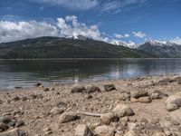 a lake with rocks on the shore and mountains in the background along side it and snow capped hills