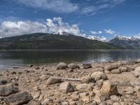 a lake with rocks on the shore and mountains in the background along side it and snow capped hills