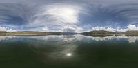 a large lake with the sky reflecting on it in a mountainous area, with mountains and clouds in the background