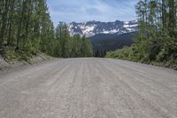 gravel road with mountain in background and tree line on the other side of it,