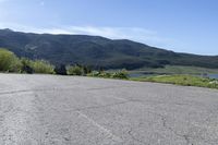 an empty parking lot with a sign near water and mountains in the background of a park