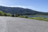 an empty parking lot with a sign near water and mountains in the background of a park