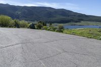 an empty parking lot with a sign near water and mountains in the background of a park