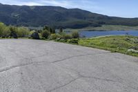 an empty parking lot with a sign near water and mountains in the background of a park