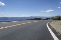 a road with mountains and yellow lines running on it, with a bicycle leaning up against it