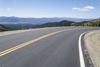 a road with mountains and yellow lines running on it, with a bicycle leaning up against it