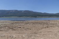 there is a body of water surrounded by mountains and rocks and dirt field, with a man on a bench in the foreground