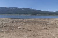 there is a body of water surrounded by mountains and rocks and dirt field, with a man on a bench in the foreground