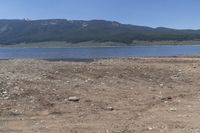 there is a body of water surrounded by mountains and rocks and dirt field, with a man on a bench in the foreground