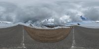 the large road stretches into the horizon in this panorama of snow capped mountains and glaciers