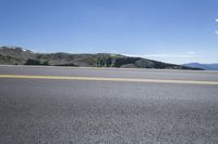 an empty highway with yellow painted double lines in the middle of the road and mountains in the background