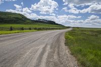 gravel road with a fence on each side with a mountain in the distance and clouds in the sky