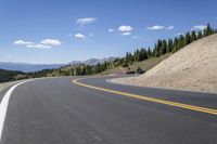 a long curved highway with mountain views in the background and people riding down it at each end