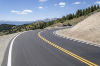 a long curved highway with mountain views in the background and people riding down it at each end