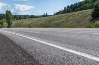 an open road is shown with a mountain in the background with trees on one side and hills on the other, near a highway