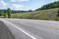 an open road is shown with a mountain in the background with trees on one side and hills on the other, near a highway