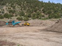 two yellow bulldozers work on sand and gravel in a mountain valley while another one looks at it