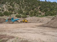 two yellow bulldozers work on sand and gravel in a mountain valley while another one looks at it