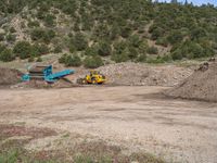 two yellow bulldozers work on sand and gravel in a mountain valley while another one looks at it