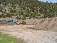 two yellow bulldozers work on sand and gravel in a mountain valley while another one looks at it