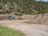 two yellow bulldozers work on sand and gravel in a mountain valley while another one looks at it