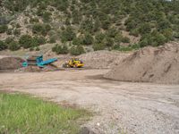 two yellow bulldozers work on sand and gravel in a mountain valley while another one looks at it