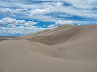 the sky has clouds in it and many large dunes are covered with sand underneath the blue skies