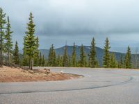 there is a black sign that is on a road with mountains in the background, on top of a hill near trees