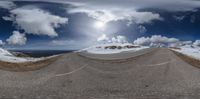 a wide angle view of a snowy road in the middle of mountains and clouds behind