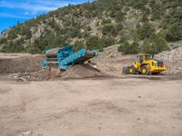 two yellow bulldozers work on sand and gravel in a mountain valley while another one looks at it