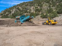 two yellow bulldozers work on sand and gravel in a mountain valley while another one looks at it