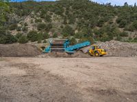 two yellow bulldozers work on sand and gravel in a mountain valley while another one looks at it