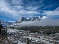 a scenic view of some snowy hills and trees with a few clouds hovering in the background