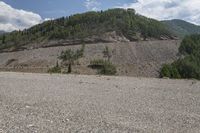 an empty road with trees on a mountain side covered in boulders and gravels in the foreground