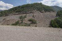 an empty road with trees on a mountain side covered in boulders and gravels in the foreground