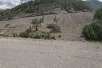 an empty road with trees on a mountain side covered in boulders and gravels in the foreground