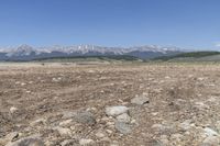 an open land with rocky mountains in the distance, with a blue sky over the valley