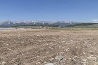 an open land with rocky mountains in the distance, with a blue sky over the valley