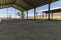 a barn with a fence and some hay, some hay and a small cow standing under it