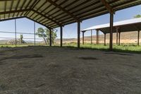 a barn with a fence and some hay, some hay and a small cow standing under it