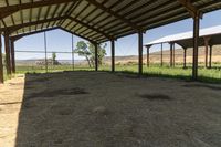 a barn with a fence and some hay, some hay and a small cow standing under it