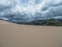 a white motorcycle riding down a large sand covered field under grey skies above mountains and trees