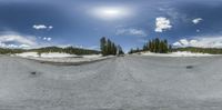 a panorama fish eye view shows the mountains below and the ground around it, with a snowboarder coming down