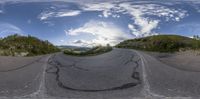 fish eye picture of a paved road with cars in the background with trees on each side and mountains in the distance