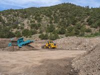 two yellow bulldozers work on sand and gravel in a mountain valley while another one looks at it