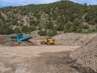 two yellow bulldozers work on sand and gravel in a mountain valley while another one looks at it